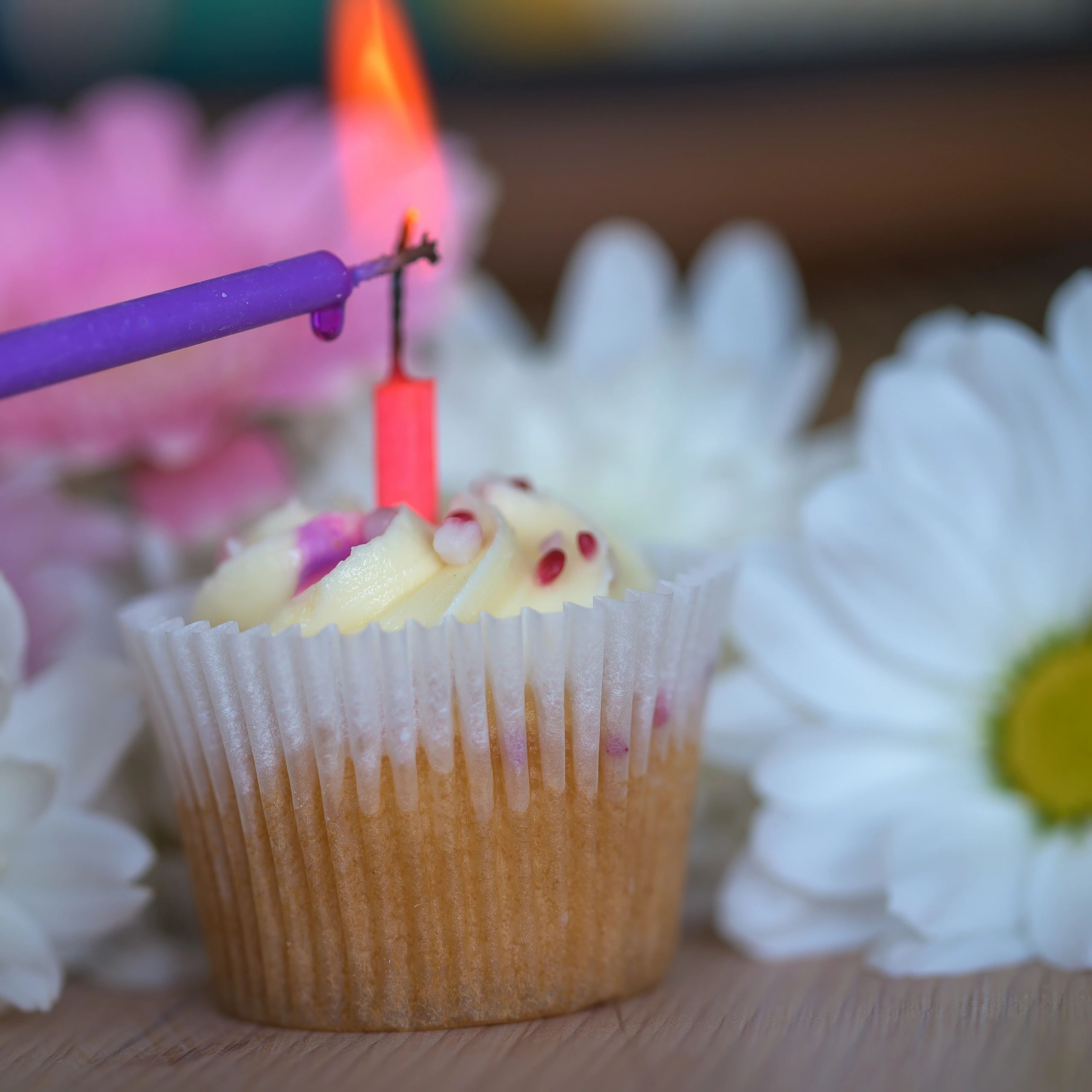 Cupcake with frosting and a lit candle on a wooden table