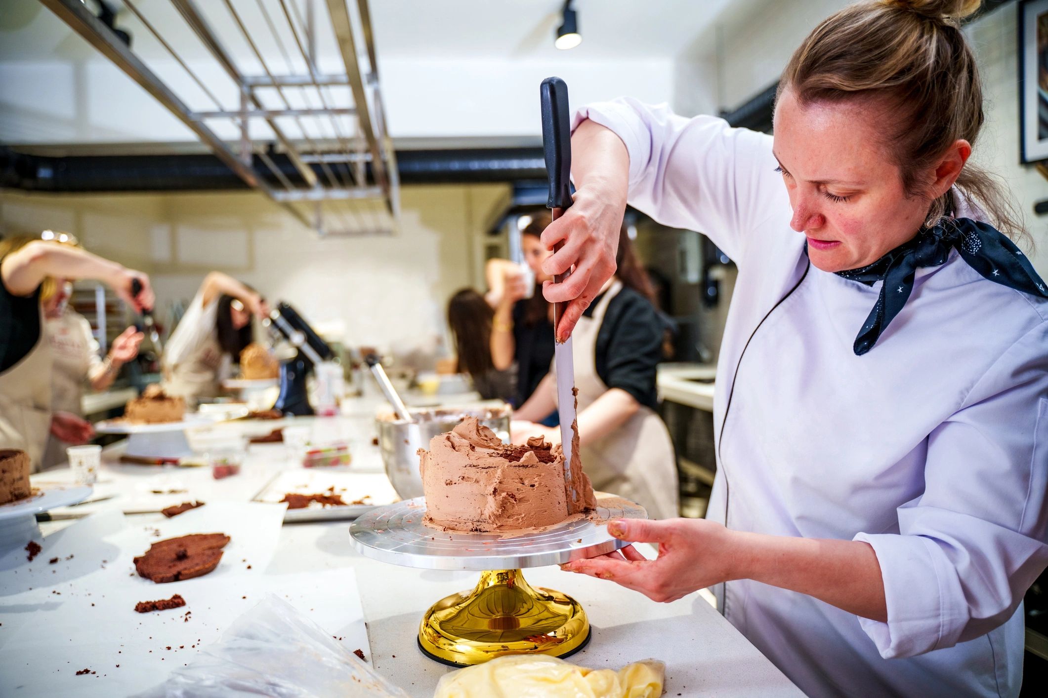 Pastry chef decorating a layered cake in a professional kitchen