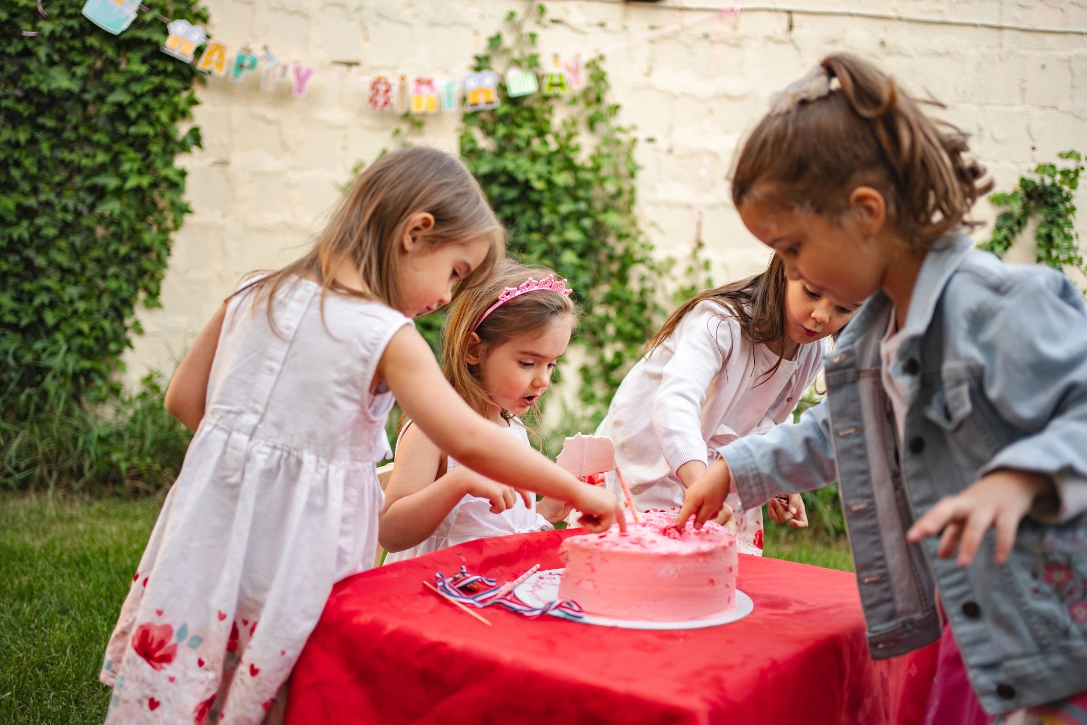 Kids tasting a pink birthday cake at a garden party