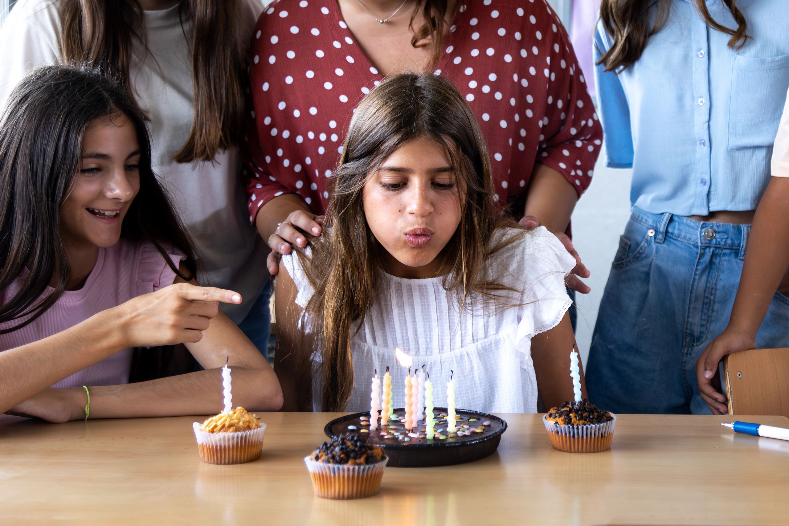 Girl blowing out candles on a birthday cake surrounded by family and friends